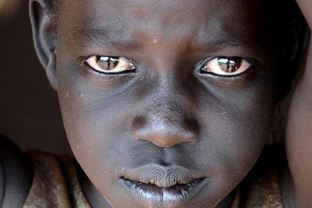 2014, Uganda. Portrait of a young  South Sudanese girl in Kiryandongo Refugee settlement. Around this time were my initial years as a commissioned photographer and I was assigned a week-long job to accompany a local NGO to the refugee settlement. This settlement, originally established in 1990 had been re-opened because of the South Sudan emergency, and the NGO I was working with was providing psycho-social support to the individuals who were dealing with the traumatic events that happened in their homeland. At that time, the country was engulfed in a civil war between forces of the government and opposition forces. The president (Kiir) accused his former deputy Riek Machar and ten others of attempting a coup détat.Like most of the fleeing families, parents are looking for a safer place for their children during such chaotic times. Between October 2014 and June 2018, the UN found that 6,500 children were recruited by both sides of the war and were subjected to many forms of abuse. © Jjumba Martin 2014