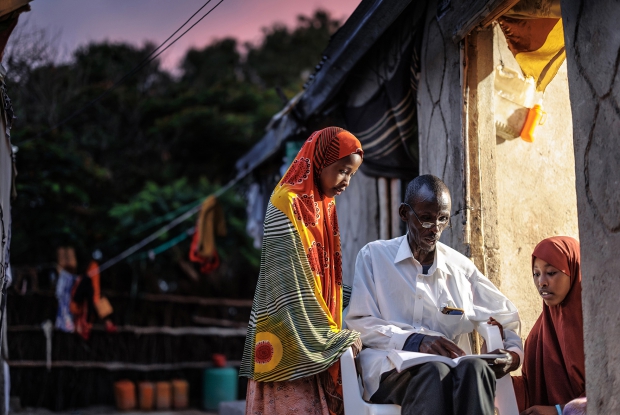 11.05.2024, Sheder refugee camp, Northeastern Fafan Zone in the Somali region of Ethiopia. - 58-year-old Muse takes two of his daughters through a school exercise with the use of light from the inside of one of the rooms in his compound.  The family of 14 has lived in the Sheder refugee camp for 10 years now, after fleeing AL Shabab in 2012. &copy; MERCYCORPS/ Jjumba Martin 2024.