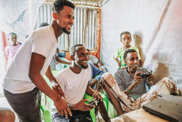 May 9th, 2024- Sheder Refugee Camp, Ethiopia. - Osman plays a game with his clients at his gaming shop in sheder.  When he started his gaming business, he couldn't get customers during day time because electricity was only available for 2-3 hours and this was in the evening hours. Having electricity supply has also enabled him to run the business all day, thus increasing his income. He has also ventured into online purchase business. The reliable power supply also ensures that his phone, which is his working gadget is always charged. &copy; MERCYCORPS/ Jjumba Martin 2024.