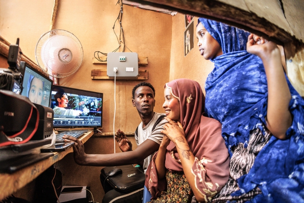 May 11th, 2024- Sheder Refugee Camp,  Northeastern Fafan Zone in the Somali region of Ethiopia. - Khadar interacts with  clients during a photo editing session at his photo studio. &ldquo;My parents say that the major reason as to why they left Somalia was because of how compromised our safety had become. I have since been staying in this Refugee Camp with my family of 16. I started and finished my studies here. Right from primary to secondary school and finally, the university studies here. Now, I own this photo studio. In this refugee camp setting, I feel like life keeps getting harder to maneuver financially, but I am glad that the idea of starting up this studio came to my mind. It has made it easier for me to contribute to my family's income. Before the solar power project came here, there was a big challenge in accessing electricity. We would pay for electricity per month but they would only switch it on for 3 hours a day. They would switch it on at 6:30 or 6:40 in the evening and then switch off at exactly 10. This is distasteful for any business that's dependent on electricity. People in this community had to go to neighboring towns where photo studios had access to electricity for services as basic as a passport photo. My business never made sense until when I knew about the plans to have us connected to a reliable source of power and since the connection, the problem has gotten behind me. People can now access my services all day and I am also making some good money. The money that I used to make in 4 days, I now make it in 1 day.