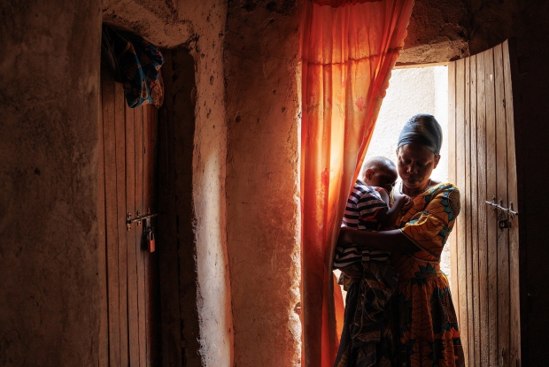 Kyaka refugee settlement - Felista enters her house with her 6-year-old daughter who cannot sit nor stand. Felista&acute;s story highlights the challenges of living in a refugee settlement or camp with disability. She tends to her daughter 24 hours a day amidst the hardships of living in a challenging environment. - &copy; Jjumba Martin, Chance for Childhood 2022