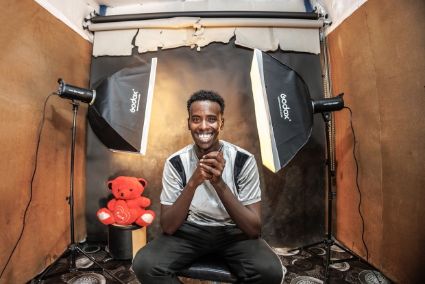 May 11th, 2024- Sheder Refugee Camp, Northeastern Fafan Zone in the Somali region of Ethiopia. Khadar Abdi sits in his photo studio. &ldquo;My parents say that the major reason as to why they left Somalia was because of how compromised our safety had become. I have since been staying in this Refugee Camp with my family of 16. I started and finished my studies here. Right from primary to secondary school and finally, the university studies here. Now, I own this photo studio.  In this refugee camp setting, I feel like life keeps getting harder to maneuver financially, but I am glad that the idea of starting up this studio came to my mind. It has made it easier for me to contribute to my family's income. Before the solar power project came here, there was a big challenge in accessing electricity. We would pay for electricity per month but they would only switch it on for 3 hours a day. They would switch it on at 6:30 or 6:40 in the evening and then switch off at exactly 10. This is distasteful for any business that's dependent on electricity. People in this community had to go to neighboring towns where photo studios had access to electricity for services as basic as a passport photo. My business never made sense until when I knew about the plans to have us connected to a reliable source of power and since the connection, the problem has gotten behind me.  People can now access my services all day and I am also making some good money. The money that I used to make in 4 days, I now make it in 1 day. - Khadar
