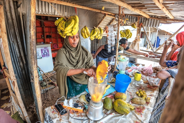 May 12th, 2024 - Sheder Refugee Camp, Amina working at her shop with her husband Abdilahi in Sheder Refugee Camp. The two operate the shop together. 33-year-old Amina Muhammad Hassan left Somalia on the 11th of November 2011 and they have been residents of the Seder camp since then with her family of 8 members. For the first time in a while, she lived in a place without conflict. However, she felt limited with movement as a refugee in Ethiopia. The other thing was how hard it was to manage the family with no financial security. To the list of challenges she faced in the refugee camp, Amina adds that for years, she and the other refugees struggled with the lack of a constant supply of electricity. &ldquo;Most of the time, I couldn't run my businesses due to the limited power supply. As a person who runs a fruit juice and grilled meat business, I needed a constant supply of electricity, if I was to record any form of business growth.&rdquo; Amina is happy for the Mercy Corps' Enter Energy Project because her business no longer has electricity challenges and, therefore makes more money. Back at home, we no longer live in the dark and my children can do homework at night. I can even charge my phone whenever necessary without having to travel to the trading center. Now, there is a fully functional hair salon in my neighborhood. On a personal level, Amina confirms that her dream of creating assets that her children can inherit has started taking shape. At her shop, Amina has a refrigerator, which stores fresh smoothies and cold water that are essential in a hot place like Sheder. The Enter Energy Program aims to improve the climate resilience of displaced populations by harnessing the power of public and private capital to deploy sustainable energy-as-a-service solutions to displaced populations, their host communities, and the humanitarian actors that support them; as well as empowering livelihoods through the productive use of energy. Humanitarian Energy aims to scale this model to 10 of the most crisis-affected countries in the next 10 years.