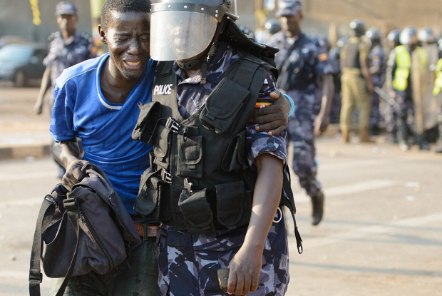 A young man is helped by a policeman after being shot with a teargas canister during a demonstration in Wandegeya. Supporters of the Forum for Democratic Change (FDC) rioted after police had blocked Kizza Besigye from accessing Makerere University where he was meant to hold a campaign. This photo won The Uganda Press Photo Award (UPPA) 1st place in the news Category that year. &copy; Jjumba Martin.