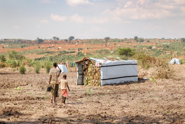Stella walks with her 6-year-old daughter towards their newly set up house in Nakivale Refugee Settlement, Isingiro district, Uganda. Stella a mother of three came to Uganda several years ago, from Rwanda, fearing for her life. She lived with local communities until recently when the Government of Uganda allocated her land in Nakivale Refugee Settlement. Each refugee family in the settlement is initially given some food rations, as well as non-food items like blankets, sleeping mats, and household shelter kits. The family is also given a small piece of land for subsistence agriculture and each season, the family is expected to be more self-sufficient and, eventually, &ldquo;phased off&rdquo; food and other humanitarian assistance. &copy; Jjumba Martin for Catholic Relief Services 2018.