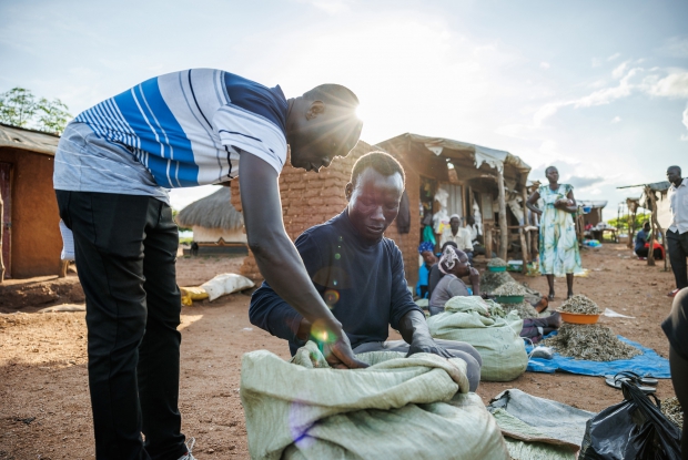 October 4th, 2022- Bidi Bidi refugee settlement. John Sanya, a Project Officer at Mercy Corps interacts with Festo James, a South Sudanese refugee, and beneficiary of the DREAMS Program that Mercy Corps is implementing in a consortium with Village Enterprise. Village Enterprise has been supporting business groups of three members with a grant to start a business and business training sessions for sustainability. This is all in a bid for the refugees to earn an income and improve their well-being. James and his two colleagues have set up this business in the local market where they sell silver fish, a popular and high-nutrient dish among the people here. &copy; Jjumba Martin, Mercy Corps 2022.