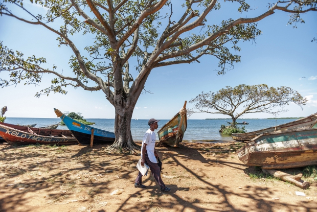 Kiriibwa Ronald, a community Health Worker, walks past boats in his community, in Kasekulo Landing site, an inland landing site and fishing village on Lake Victoria. "As a Community Health worker, one of my responsibilities entails educating my community on water sanitation, family planning and malaria prevention.  I also treat children aged five and below. The 130 households that I visit every month know that I am their quickest link to the nearby  Health Facilities every time an acute illness attacks their children. I am proud of helping my community fight preventable sickness.