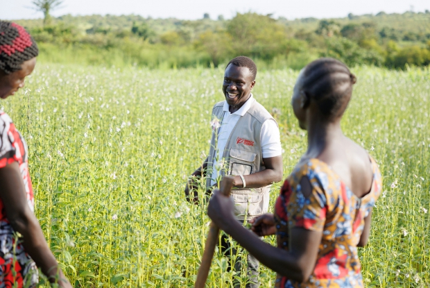 John Sanya, a Project Officer with Mercy Corps, interacts with the members of the Unit Business Group during a courtesy field visit to their sesame garden. Under the DREAMS program, the business group received financial support, which they used to hire about 3.5 acres of land to grow sesame. Additionally, all three women received training in running an agribusiness enterprise and being able to earn from it.