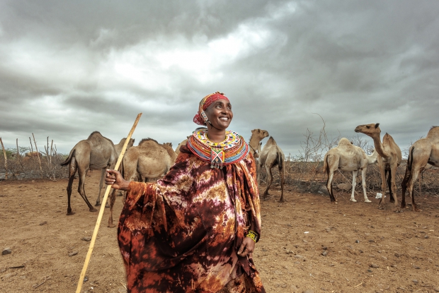 13/03/2025 Marsabit County, Kenya - Galmisan Ngurusi stands proudly in front of her camel. In a community where camels are a symbol of wealth and status, owning such has always been the domain of men. 43-year-old Galmisan Ngurusi, a mother of 7 children, has changed that narrative since she was introduced to some skills of business under the Gender Action Learning Systems. Together with two other women, they took a loan from their VSLA to start a retail shop business, and they were able to repay the money.  Galmisan further took a personal loan to purchase her first camel, which is currently pregnant.