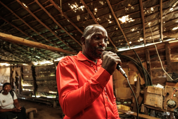 Mugisha Richard, 42, the Local Council Chairperson of the Lwabaswa-Buvuma landing site and fishing village in Kalangala District, speaks through the public address system inside a makeshift private cinema hall.  These cinemas have loud speakers that can broadcast sound to the whole landing site and inform them about different health programs in the community.  Richard offers communication and mobilization support to Nantumbwe Judith, the Community Health Worker.